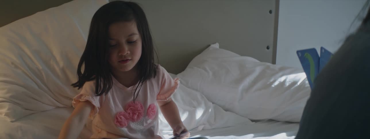 A young girl is sitting on her bed and playing a card game with an adult angrily throwing down a card