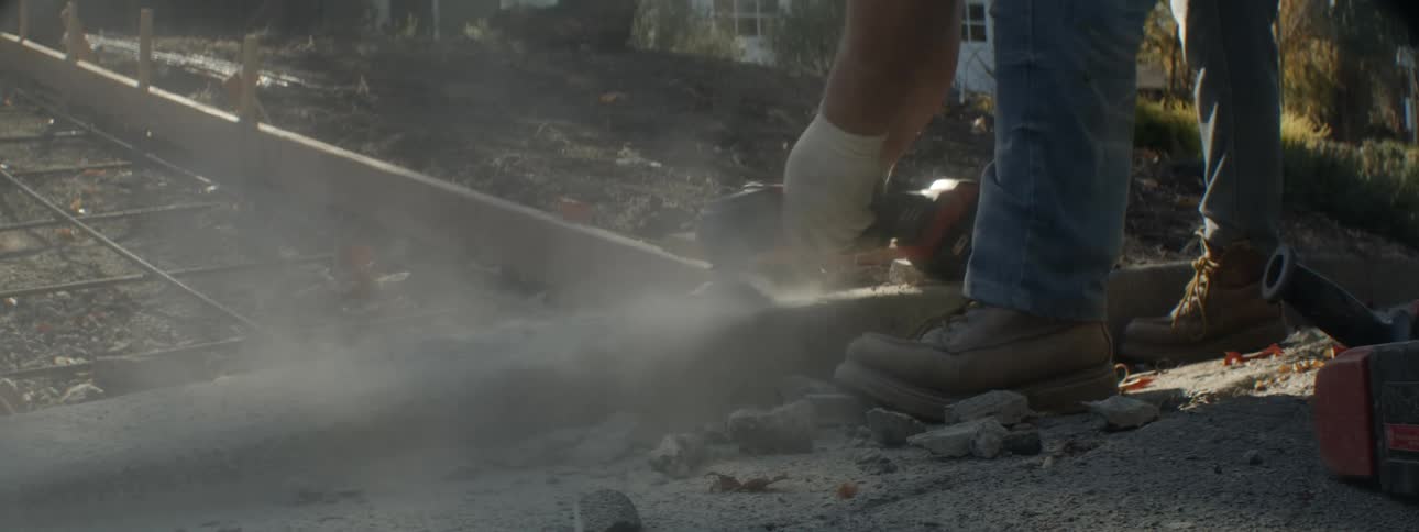 Man uses handheld power tool to smooth curve near framework prepared for the pouring of driveway
