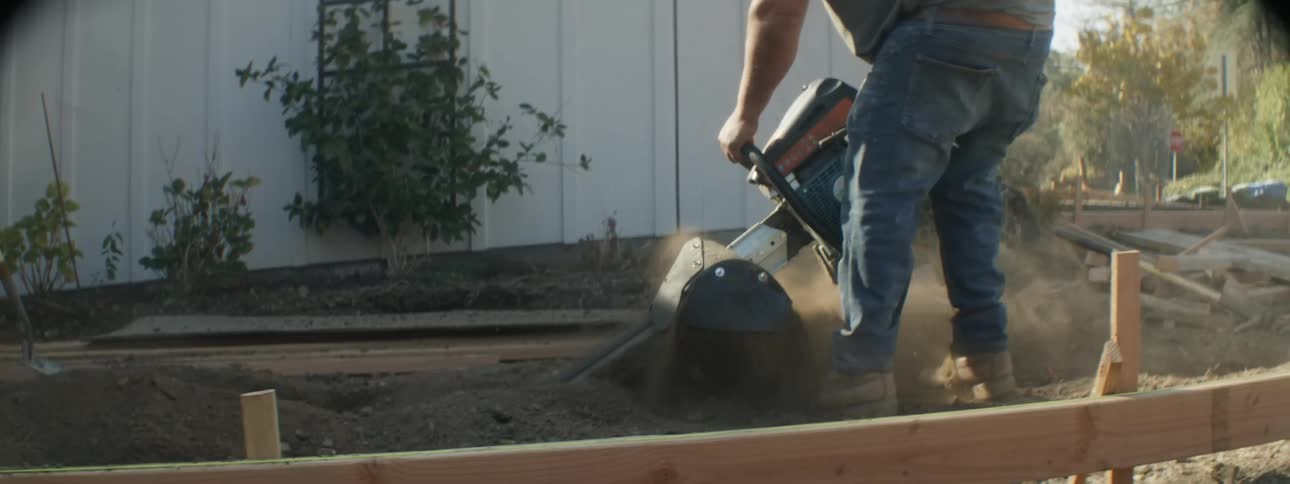 Man cuts ground with chainsaw while forming paths with wooden frame in frontyard