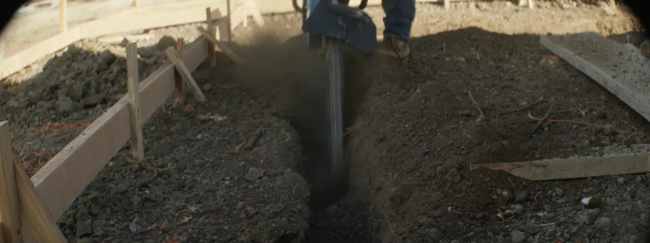 Construction worker uses a power tool to dig a trench on a construction site