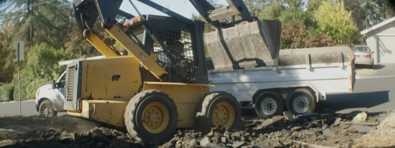 A bulldozer dumps dirt into the bed of a pickup truck