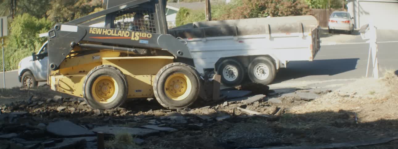 A construction loader picking up rubble from a suburban street and loading it into the back of a pick up truck