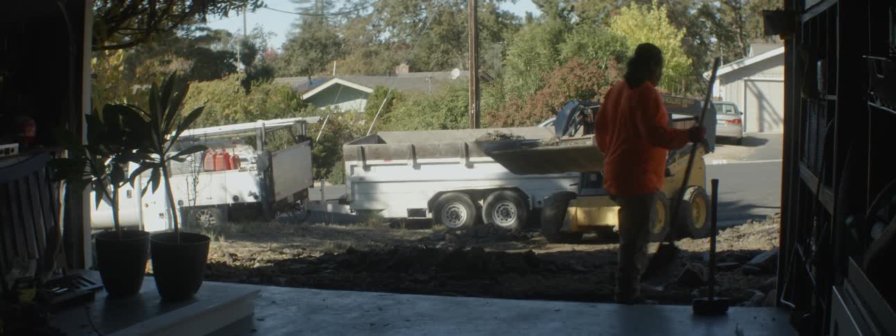 A caterpillar tractor picks up dirt from a suburban street and dumps it into the back of a truck