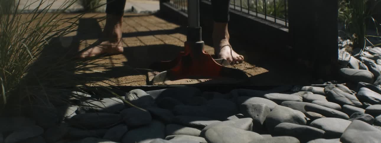Barefoot woman tamps ground while installing stone path