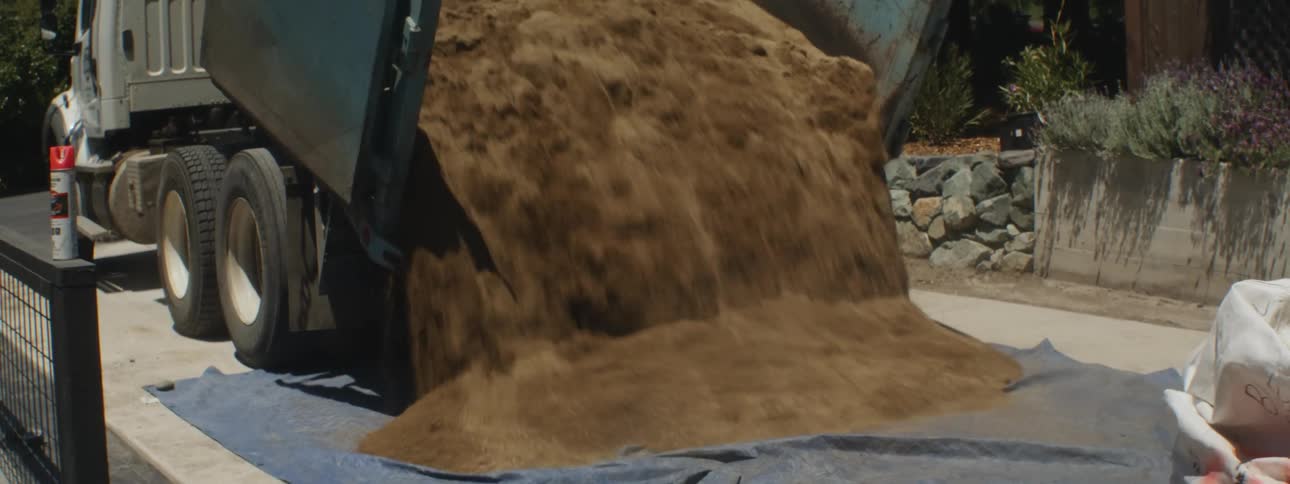 A dump truck dumping dirt onto a tarp in the middle of a street