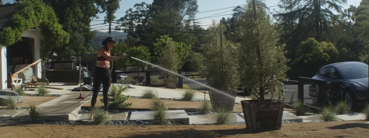 A woman waters trees in her front lawn
