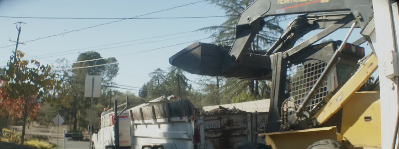 A man uses a bulldozer to dump dirt into the back of a truck
