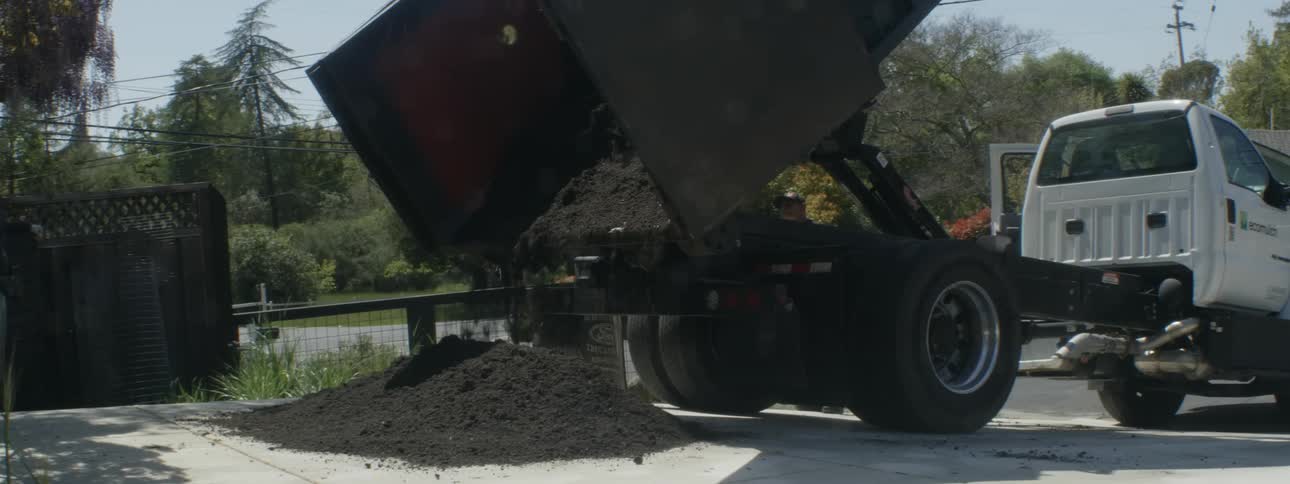 Dump truck elevates back to empty dirt onto driveway of home