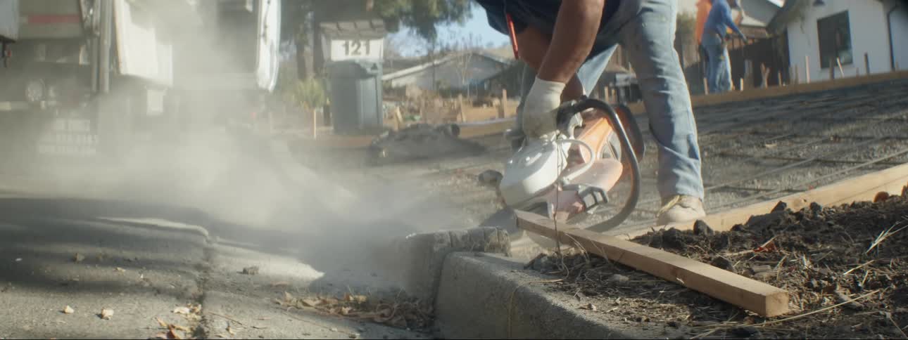 A man uses a circular saw to break apart a sidewalk