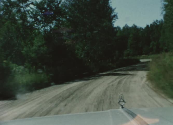 A vehicle drives down a dirt road through the woods