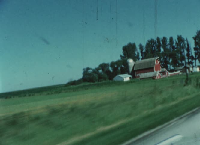 A farm with a large red barn is located right along side of a road