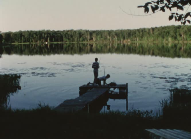 Two boys fishing on a pier on a lake at morning caught on vintage film
