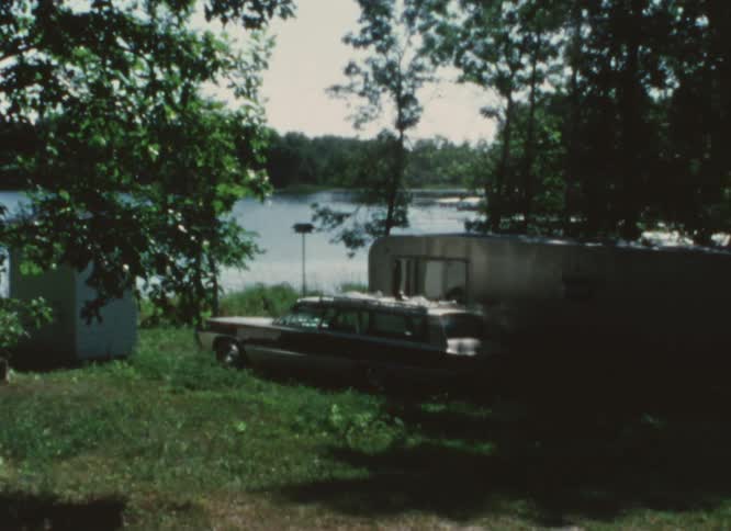 Car and trailer parked near a lake on a vacation spot caught on vintage film