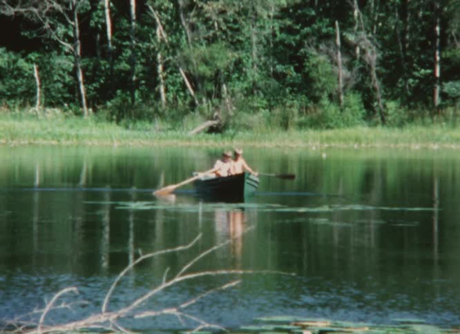 Two young boys work together to paddle a row boat around a lake