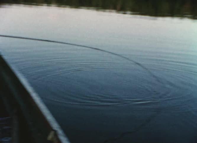 A person on a boat fishing on a lake at evening caught on vintage film