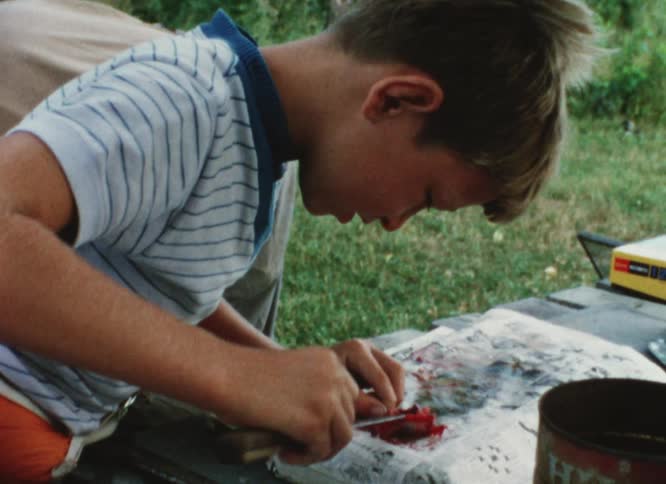 Boy learning how to gut a fish on a camping trip caught on vintage film