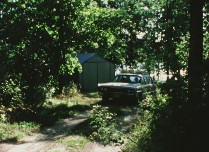 Station wagon drives on a dirt road near a lake caught on vintage film