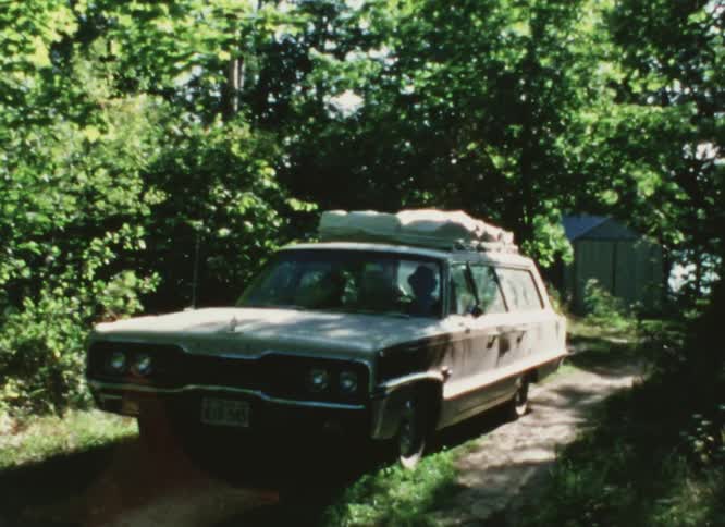 Station wagon drives on a dirt road on a rural area caught on vintage film