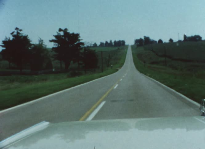 The hood of a car as it drives down a road past a grassland