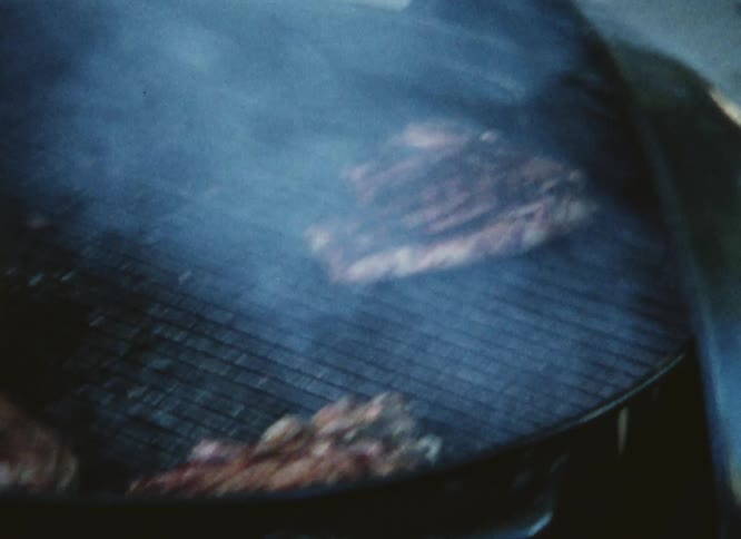 Pork chops are cooking on a smoking grill and the cook is using tongs to take them off the grill