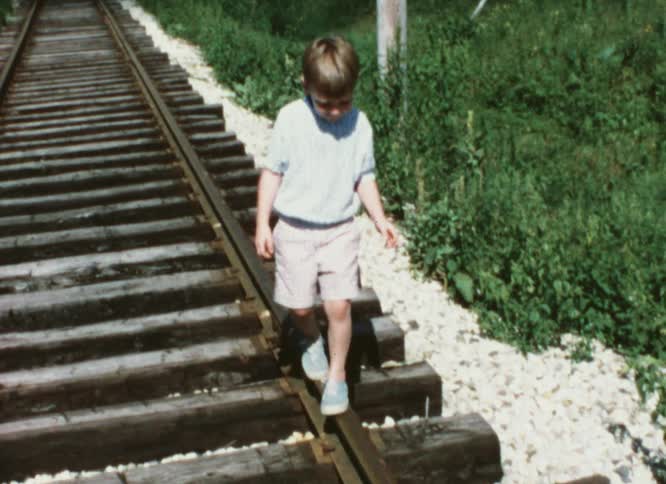 Boy wearing shorts balances while walking on railroad tracks