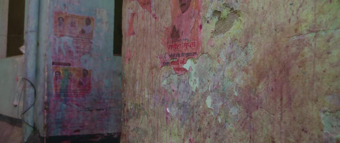 A paintsplattered wall with a poster on it written in an indian language