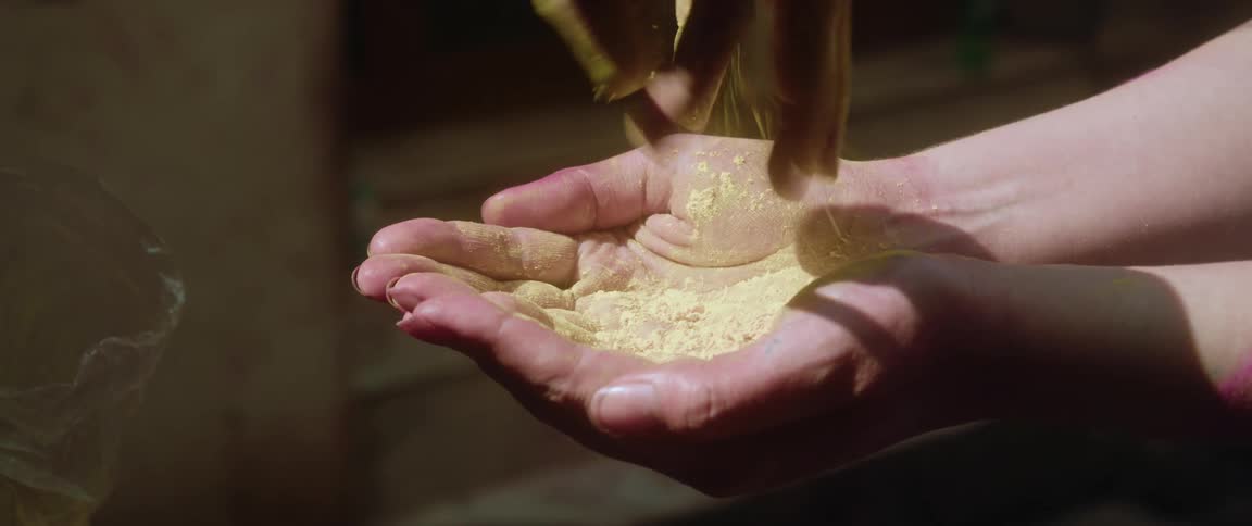 Sun shines on a womans hands as yellow powder falls into her palms and she folds her hands together