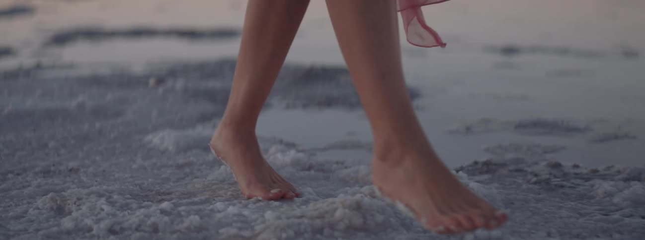 Woman wearing sheer fabric walks along the beach at sunrise