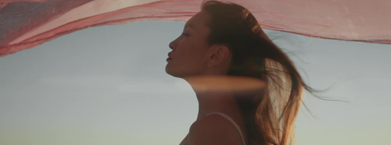 A woman lets the wind shake a sheer pink veil over her head