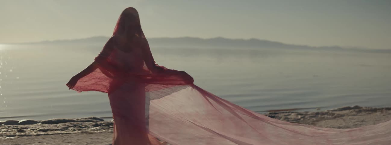 An indian woman on a beach with a sheer dress spins around wrapping herself in a long veil