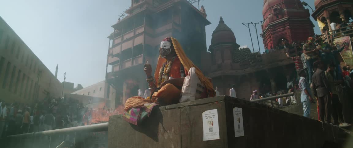 Woman wearing mask and hair covering sprays her face as fire smokes in area surrounded by historic buildings and people