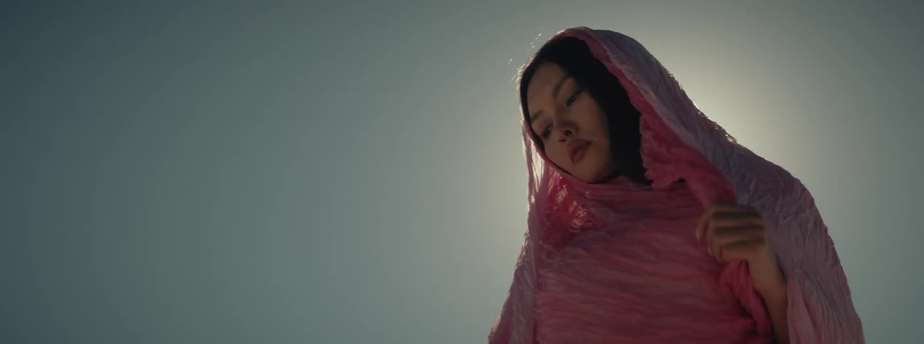 A woman looks pensive while wrapped in a sheer pink veil