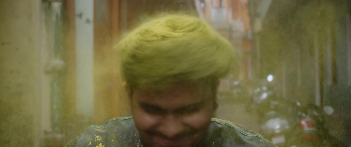 A teenage boy with yellow dye in his hair laughs as he shakes his head and the dye goes everywhere