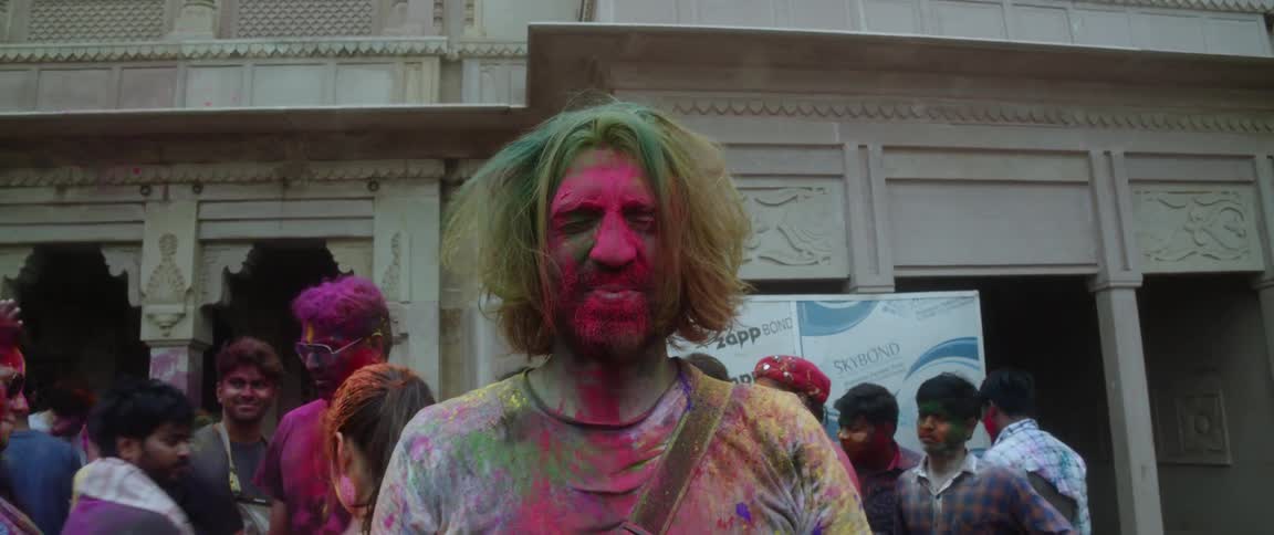 A man smiles after a man covers his face in pink powder for holi