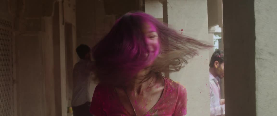 A woman with dye on her face and hair shakes her hair wildly while smiling