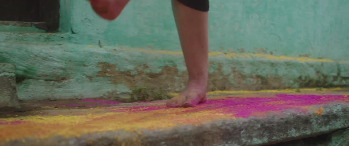 A pair of feet playfully kick powdered dye off a stone floor