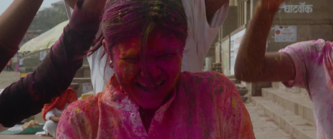 A teenage girl laughs as boys dump colored powder all over her head