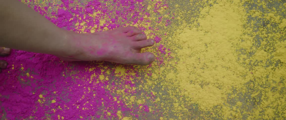 A woman walks barefoot through colorful powders on the ground