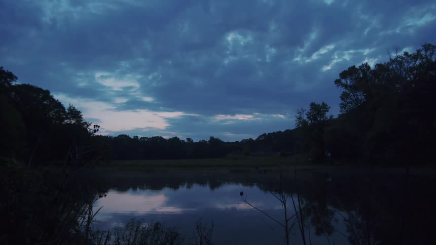 Landscape of serene lake and trees being silhouetted against the cloudy sky