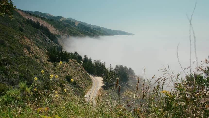 Car sits parked on highway at base of mountain as fog fills valley