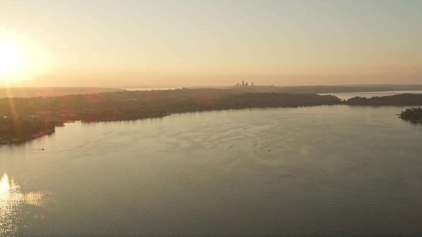 Aerial footage of the sun setting over Lake Washington as it approaches the downtown Seattle skyline in the distance