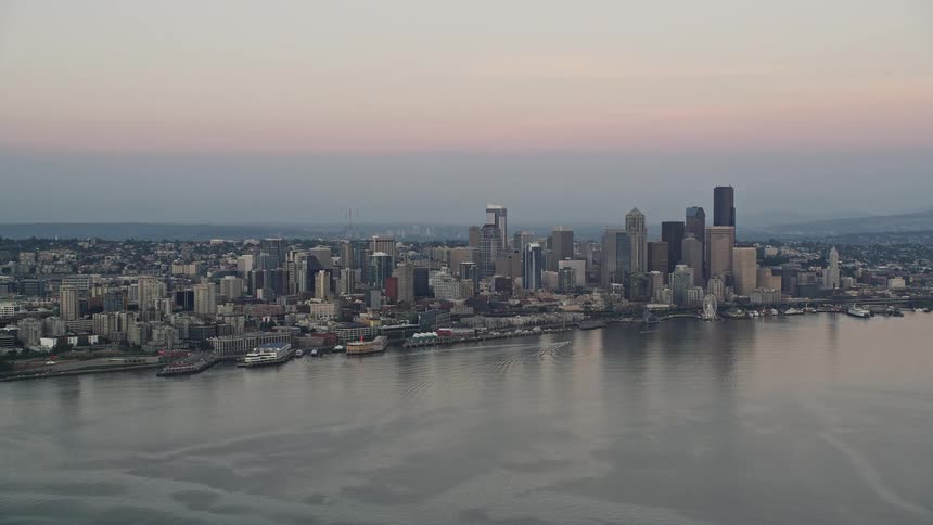 Aerial footage of Central Waterfront and Downtown Seattle skyscrapers during sunset showcasing the vibrant city skyline against the backdrop of Elliott Bay