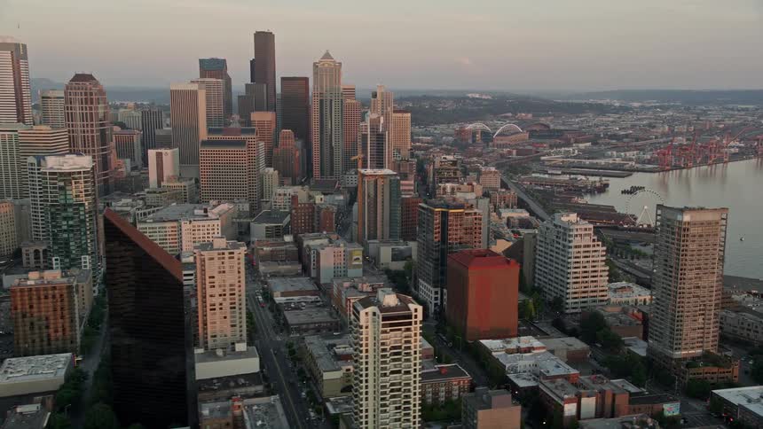 Aerial view of Downtown Seattle skyscrapers at sunset revealing the Central Waterfront piers and shoreline
