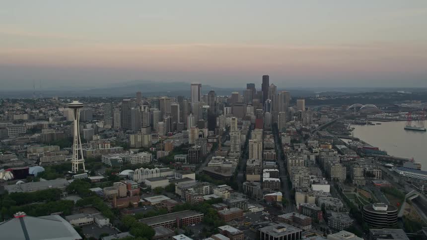 an aerial view of Downtown Seattle at sunset orbiting around the iconic Space Needle to reveal the towering skyscrapers in this bustling metropolis