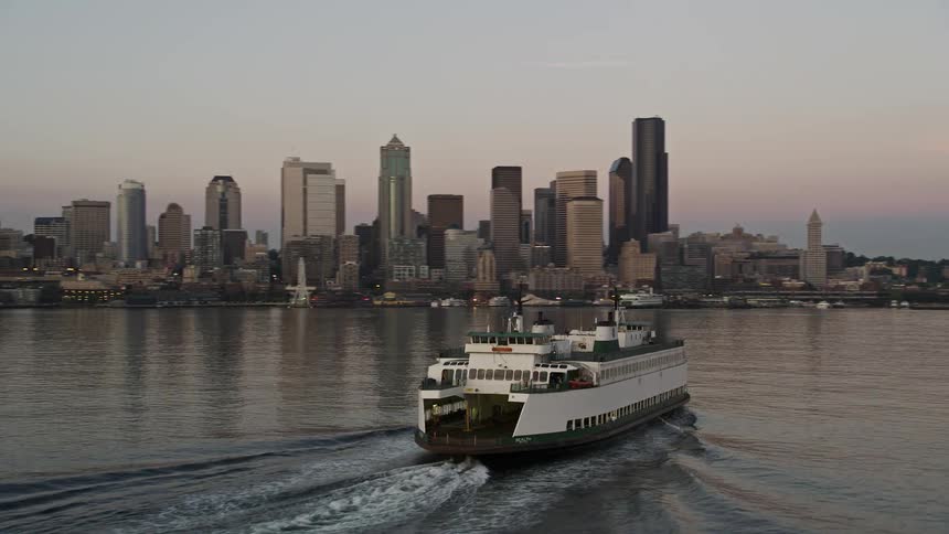 A ferry sails past downtown skyscrapers and reveals the Central Waterfront during sunset in Seattle Washington