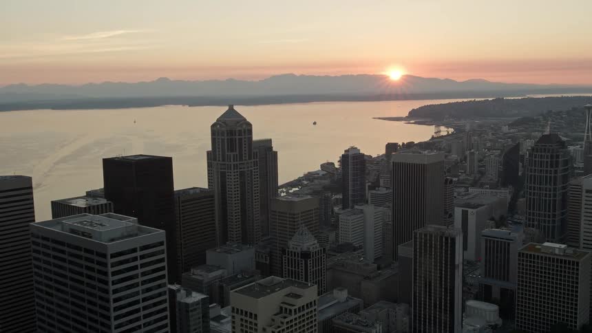 an aerial view of downtown Seattle skyscrapers and the setting sun over Elliott Bay as cars drive down the highway below