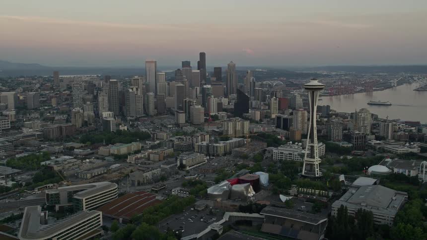 Aerial footage of Seattle's iconic Space Needle and downtown skyscrapers at sunset revealing the bustling metropolis below