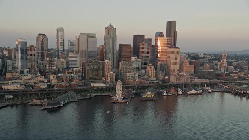 Aerial footage of Downtown Seattle skyline Alaskan Way Viaduct and Central Waterfront piers at sunset overlooking the harbor and cityscape