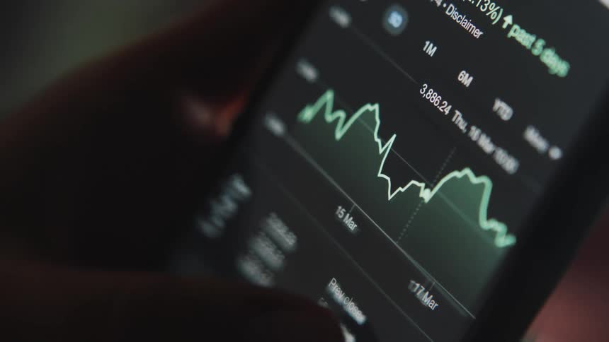 A person uses a smart phone to check the price history graph of a stock
