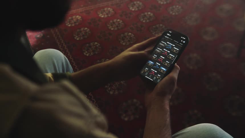 A man is sitting down holding his cell phone with both hands as he scrolls